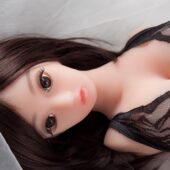 Realistic love doll with long dark hair and black lace lingerie lying on bed.